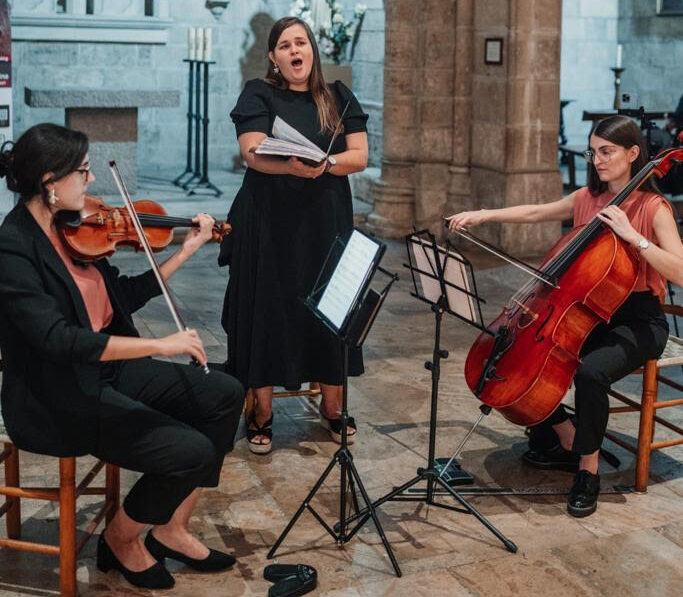 Una soprano cantando en una iglesia acompaña de un violonchelo y un violín.